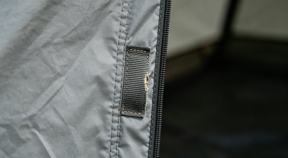 Detail close-up of reinforced door edge on blue relief tent tarpaulin, wear strip and double stitching reinforcement visible showing high-traffic area durability enhancement for long-term emergency shelter use