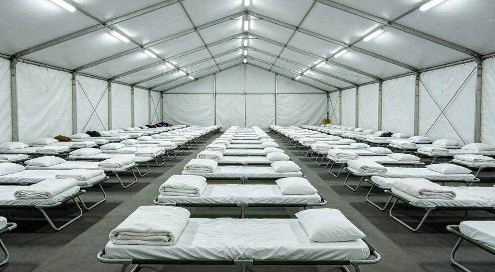 Large emergency shelter hall with rows of beds and institutional bedding Large emergency shelter hall with rows of beds and institutional bedding