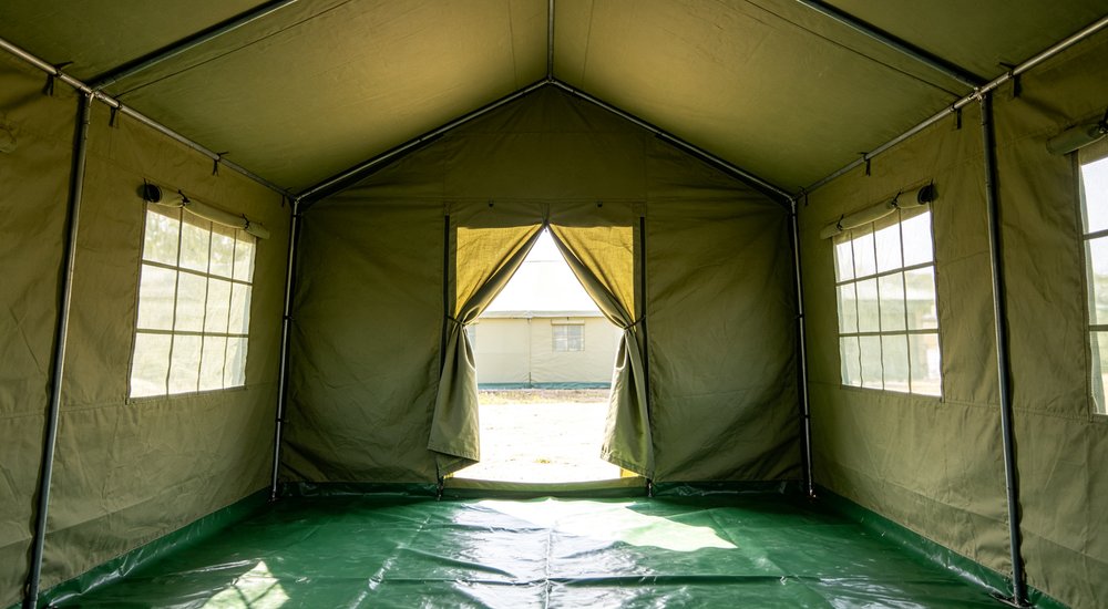 Interior upward view of beige relief tent ventilation system design, roof vents and mesh windows visible from inside showing air circulation architecture for hot humid tropical climate emergency shelter comfort
