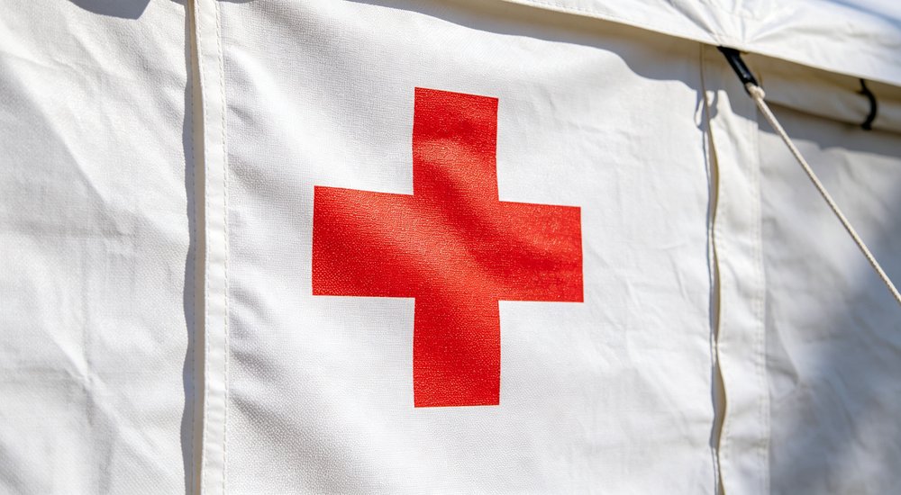 Humanitarian organization photograph showing white emergency relief tent with Red Cross logo installed at disaster site, medical emergency shelter with humanitarian organization branding visible for international disaster response operations