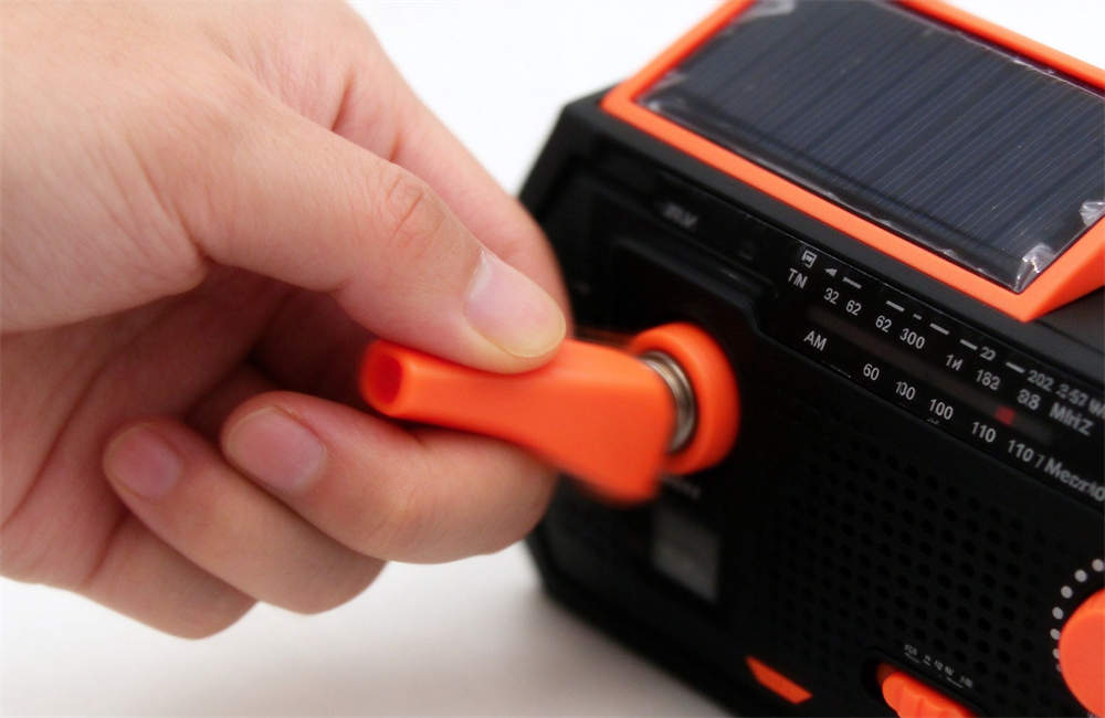 Close-up of hand crank radio handle being turned with motion blur, showing hand-powered charging mechanism that works without batteries or electricity during outages