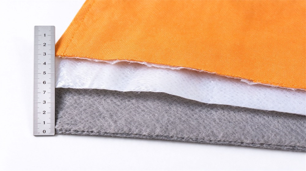 Close up studio shot showing three layer structure of firefighter turnout gear: Nomex outer shell, moisture barrier and thermal liner, layered fabric samples on light gray background