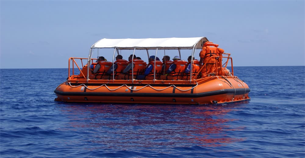 Wide view of enclosed orange life raft with survivors in open ocean showing maritime abandonment and survival
